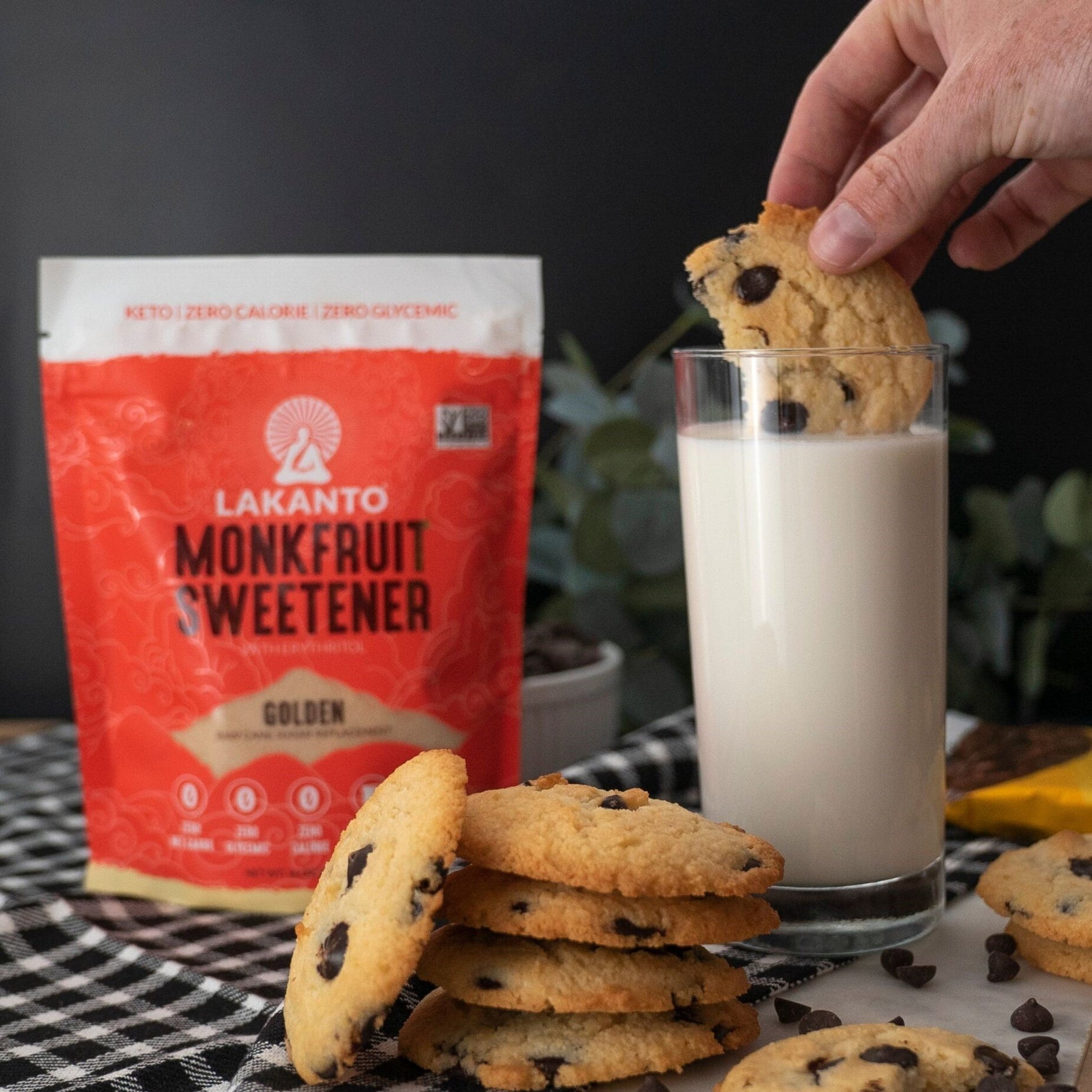Lakanto 羅漢果甜味劑 Golden 使用情境圖，畫面展示 Lakanto Monkfruit Sweetener Golden 包裝置於桌面，旁邊有朱古力曲奇及一杯牛奶，呈現甜點與飲品的日常搭配烘焙場景；Lakanto Monkfruit Sweetener Golden lifestyle image showing the product bag on a table with chocolate chip cookies and a glass of milk in a baking and snack setting.
