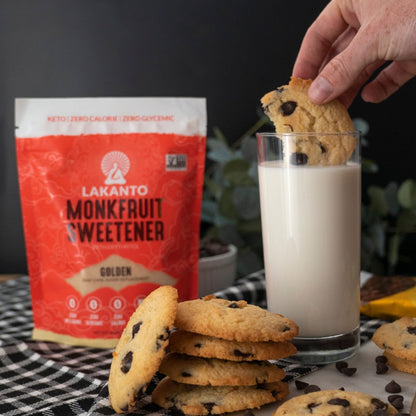 Lakanto 羅漢果甜味劑 Golden 使用情境圖，畫面展示 Lakanto Monkfruit Sweetener Golden 包裝置於桌面，旁邊有朱古力曲奇及一杯牛奶，呈現甜點與飲品的日常搭配烘焙場景；Lakanto Monkfruit Sweetener Golden lifestyle image showing the product bag on a table with chocolate chip cookies and a glass of milk in a baking and snack setting.